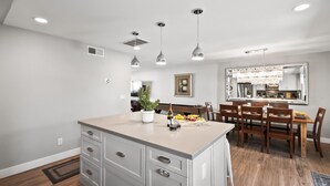 A modern kitchen with a central island, pendant lighting, and a dining area with wooden chairs and a table. - Old Town Pool Home: Patio Bar (Scottsdale)
