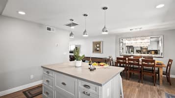 A modern kitchen with a central island, pendant lighting, and a dining area with wooden chairs and a table.