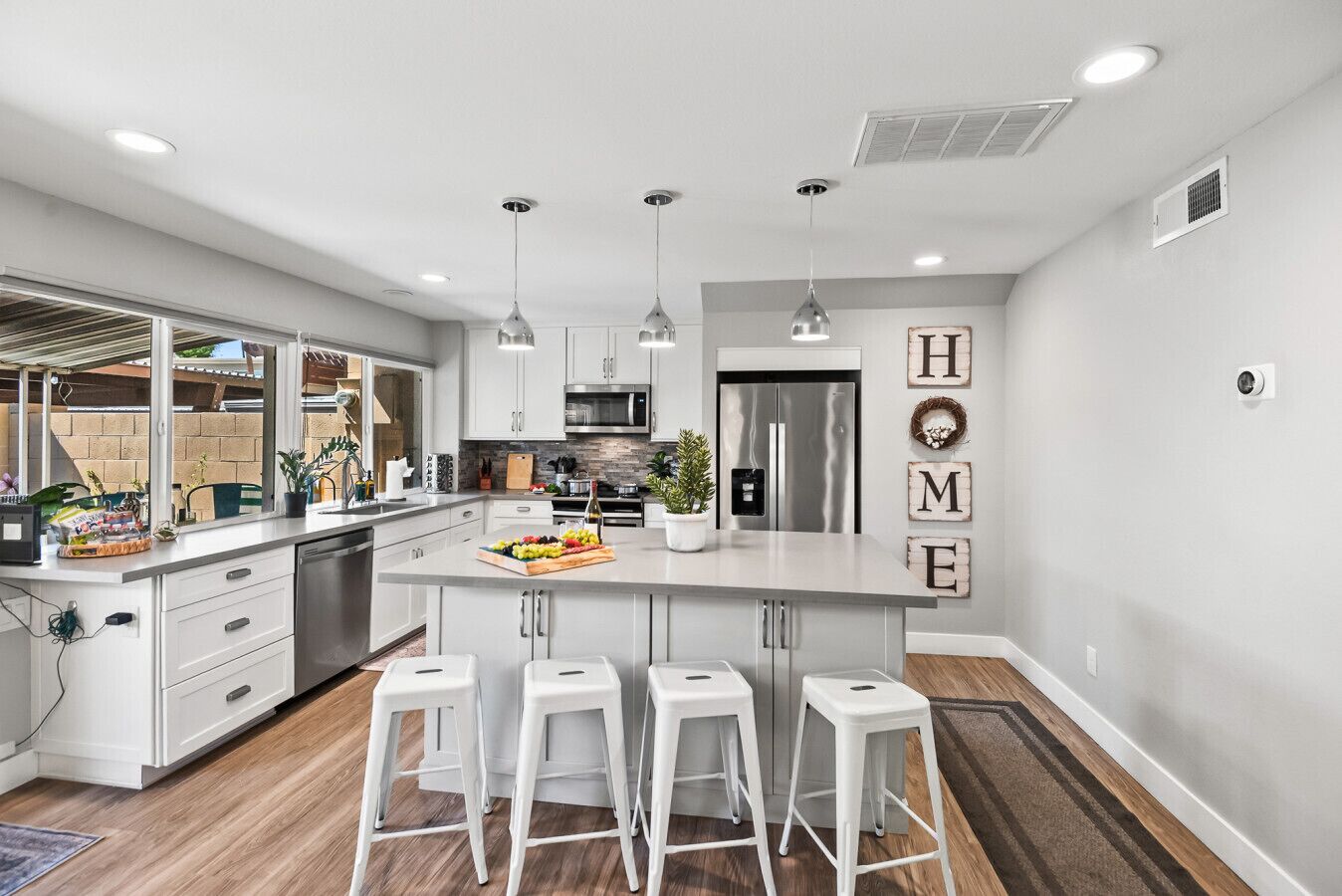 A modern kitchen with white cabinetry, a central island with bar stools, stainless steel appliances, and a view of the backyard.
