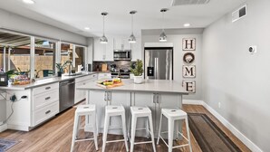 A modern kitchen with white cabinetry, a central island with bar stools, stainless steel appliances, and a view of the backyard. - Old Town Pool Home: Patio Bar (Scottsdale)