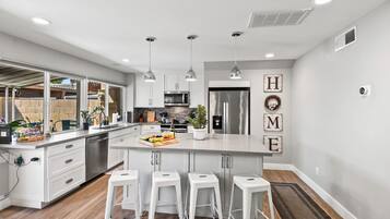 A modern kitchen with white cabinetry, a central island with bar stools, stainless steel appliances, and a view of the backyard.