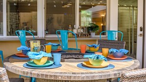 A round table with colorful plates and cups, blue chairs, and a wicker basket. - Old Town Pool Home: Patio Bar (Scottsdale)