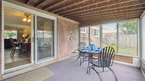 A covered patio with a table and chairs, a sliding glass door leading to a dining area, and a view of the backyard. - Family Friendly 4 Beds/Sleeps 6 In Peaceful Westland (Westland)