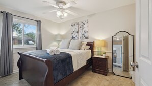 A bedroom with a wooden bed, a ceiling fan, a bedside table with a lamp, a mirror, and artwork on the wall. - Family Friendly 4 Beds/Sleeps 6 In Peaceful Westland (Westland)