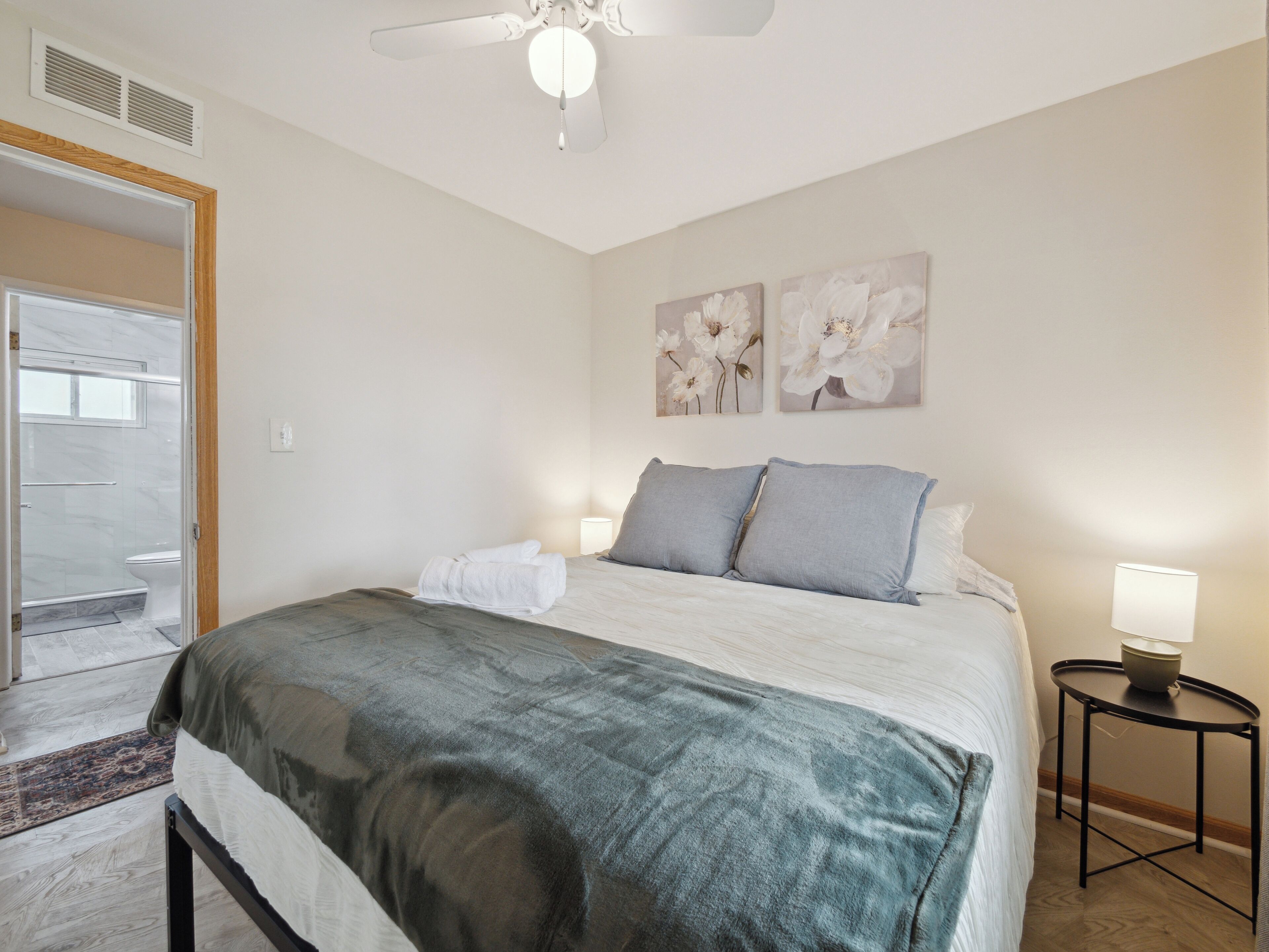Une chambre d’hôtel comprenant un lit, une table de chevet avec une lampe, un espace douche et deux œuvres d’art florales décorant le mur.