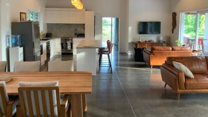 A spacious living area with a wooden dining table, a leather sofa, and a kitchen with white cabinets and a large island.