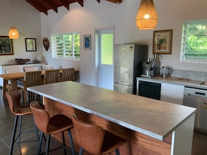 Cozinha moderna com ilha central, banquetas, frigorífico, máquina de café e máquina de lavar loiça.