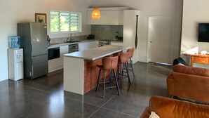 A modern kitchen with a central island, bar stools, a refrigerator, and a water dispenser.