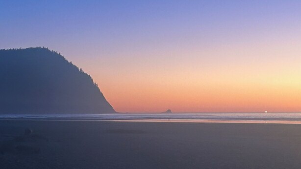 Una playa con una montaña al fondo y un cielo despejado.