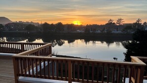 Terraza de madera con barandillas que da a un lago tranquilo al atardecer.