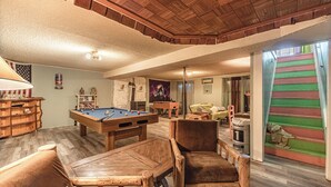 Ein Billardtisch, Holzstühle, ein Billardständer und eine Treppe mit bunten Stufen.