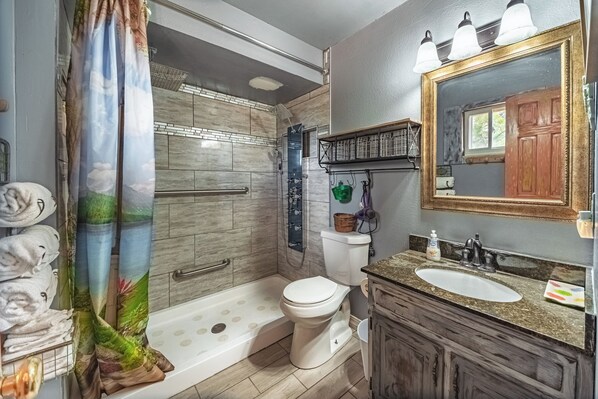 Een badkamer met douche, toilet, wastafel en spiegel.