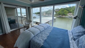 Un dormitorio con una cama grande, una silla y un balcón con vistas a un lago y edificios.