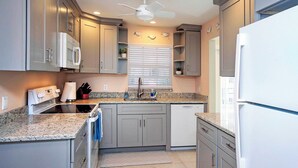 A modern kitchen with grey cabinets, a granite countertop, a built-in oven, and a ceiling fan. - Captain's Haven Sanibel, with Pergola on East End (Sanibel)