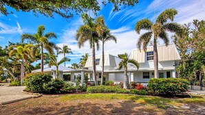 A two-story white building with a covered patio area, surrounded by palm trees and well-maintained gardens. - Captain's Haven Sanibel, with Pergola on East End (Sanibel)
