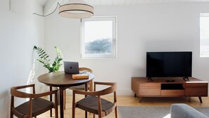 A modern living room with a wooden dining table, two chairs, a laptop, a television, and a plant. - Porto D'Alma - Infante D.Henrique - T1 (Porto)