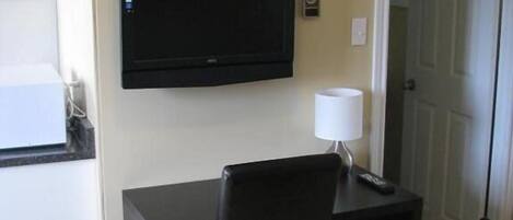 A small, dark-colored desk with a chair and a television mounted on the wall.