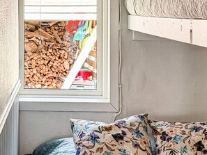 A room with a window overlooking a pile of firewood, a bed with floral-patterned pillows, and a white wall. - 7 Person Holiday Home in Hestra (Hestra)