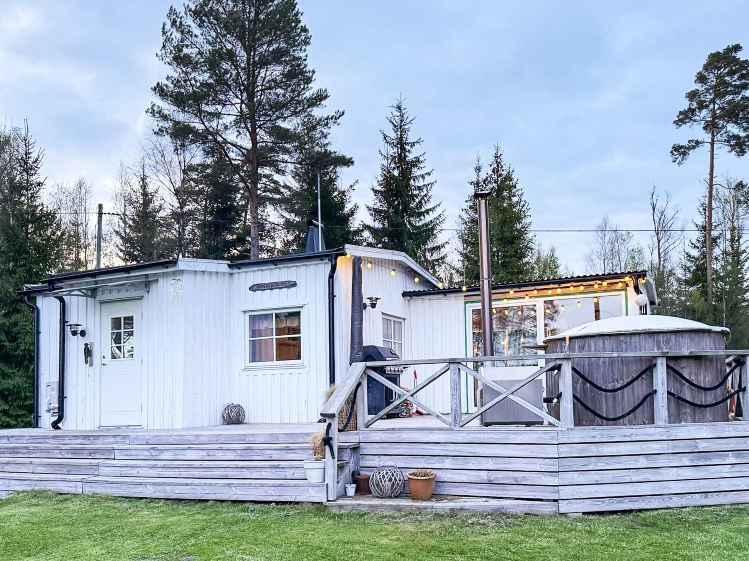 A white wooden cabin with a porch, a chimney, and a small deck area.
