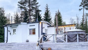 A white wooden cabin with a porch, a chimney, and a small deck area.