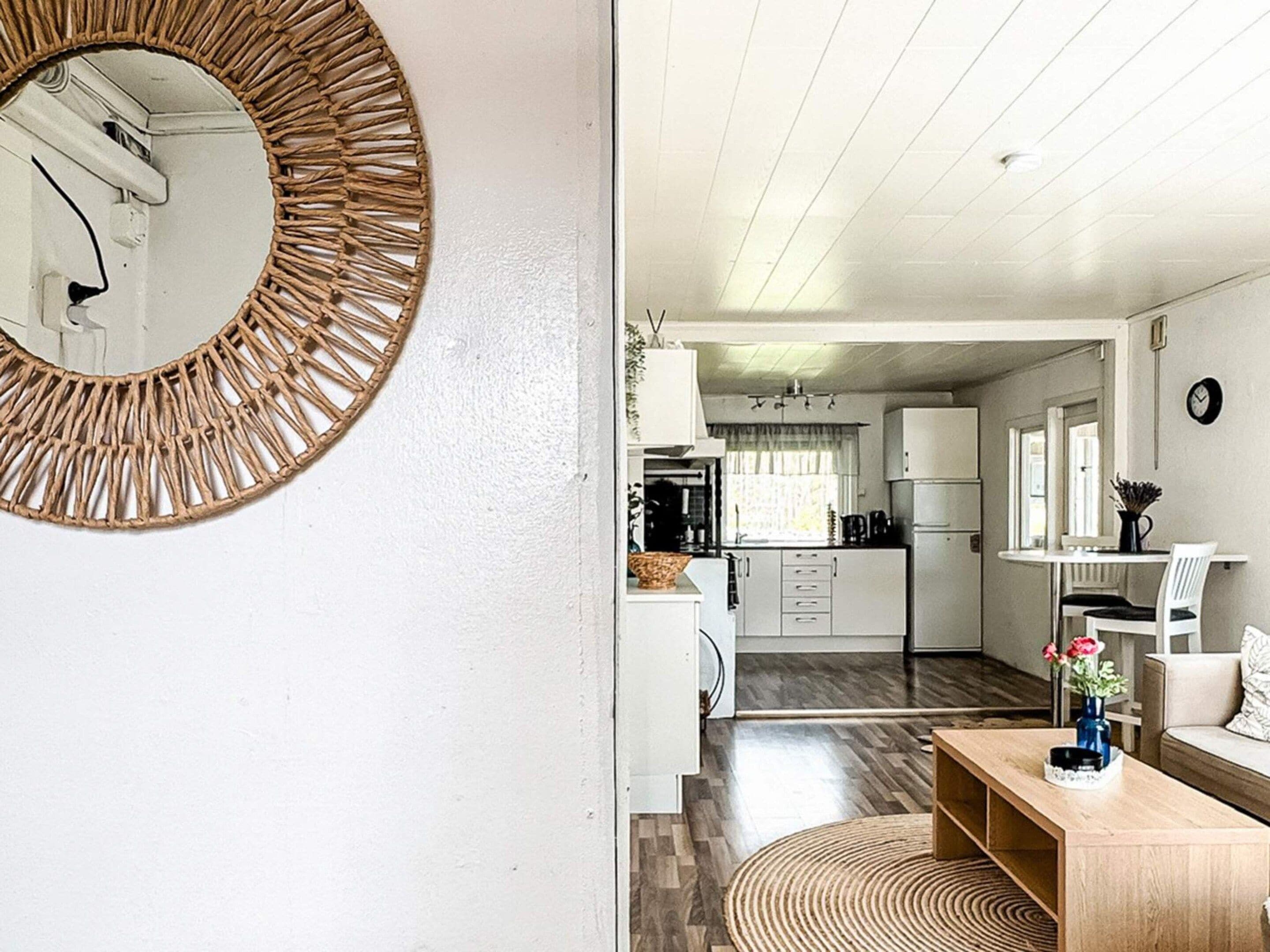 A modern kitchen with white cabinets, a wooden dining table, and a round mirror on the wall.