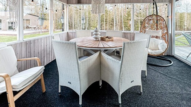 Um quarto aconchegante com uma mesa de madeira redonda, cadeiras de vime branco e uma cadeira suspensa com almofada estampada.