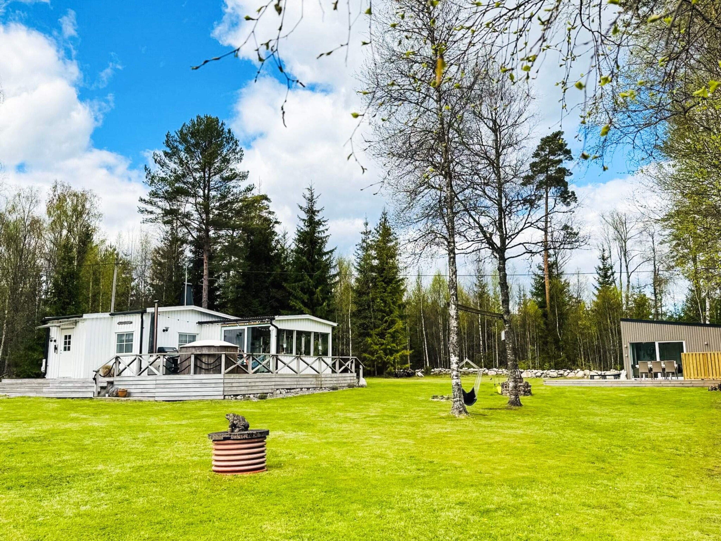 A cabin with a deck, surrounded by a grassy yard and tall trees.