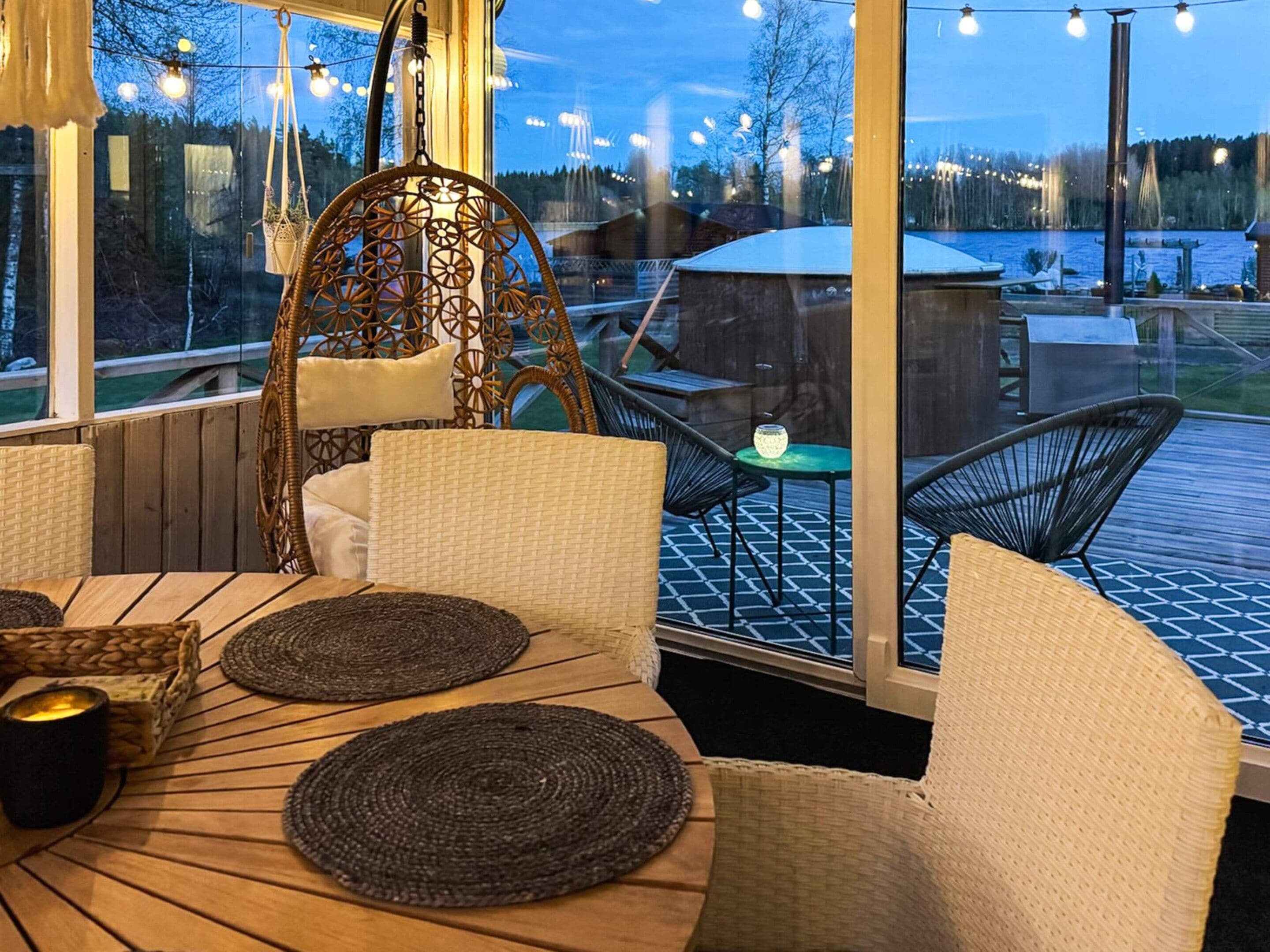 Un espacio de descanso al aire libre con mobiliario de mimbre, una silla colgante y vistas a un lago.
