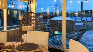 A cozy outdoor seating area with wicker furniture, a hanging chair, and a view of a lake at dusk. - 7 Person Holiday Home in Hestra (Hestra)