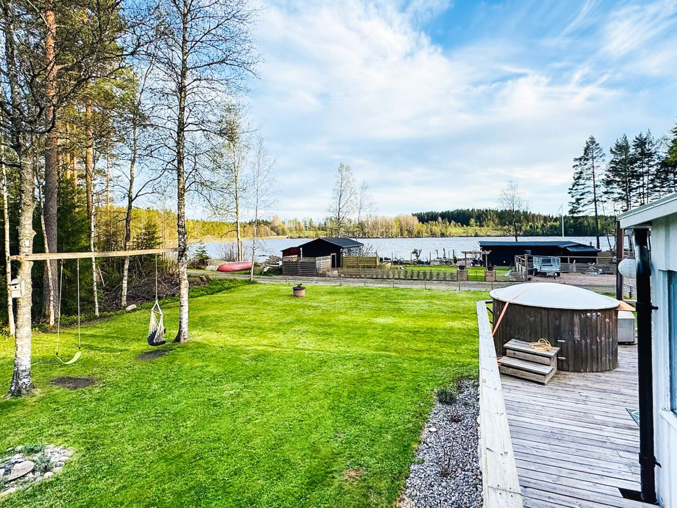 A backyard with a swing set, a wooden deck, and a view of a lake and buildings in the distance.