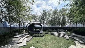 A circular seating area with a central sculpture, surrounded by a landscaped garden with grass and stone paths. - Scarletz Suites KLCC By Numa (Kuala Lumpur)