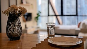 A table with a glass vase of flowers, a glass of water, and a plate. - Scarletz Suites KLCC By Numa (Kuala Lumpur)