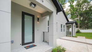 Una casa moderna con porche delantero, una puerta con panel de vidrio y un pequeño jardín.