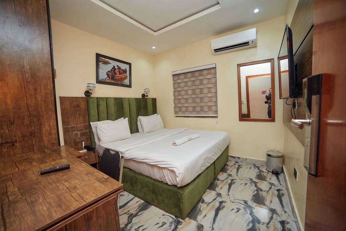 Une chambre d’hôtel avec un lit, un bureau en bois, une télévision et une poubelle.