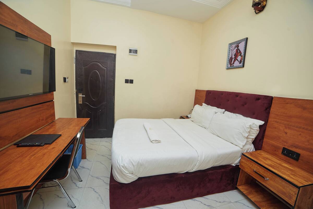 Une chambre d’hôtel avec un lit, un bureau, une chaise, une télévision et une porte.