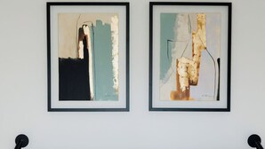 A neatly made bed with white and mustard pillows, two framed abstract paintings on the wall, and a headboard with a grey fabric. - Porto D'Alma - Marques da Silva - T1 (Porto)
