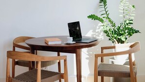 A round wooden table with a laptop, a book, and a cup. There are two wooden chairs with woven seats. A potted plant is beside the table. - Porto D'Alma - Marques da Silva - T1 (Porto)