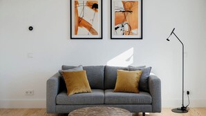 A modern living room with a grey sofa, two framed abstract paintings, a round coffee table, and a floor lamp. - Porto D'Alma - Marques da Silva - T1 (Porto)