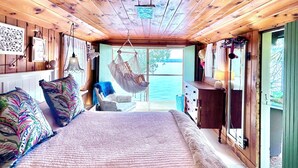 Un dormitorio de cabaña de madera con una cama grande, un sillón colgante y vistas al exterior.