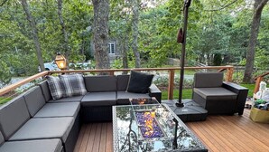 An outdoor deck with a large sectional sofa, a glass-top table with a fire feature, and a metal lantern. - Spacious, Family-Friendly Edgartown Home – 3BR, Sleeps 14, Renovated in 2025 (Edgartown)