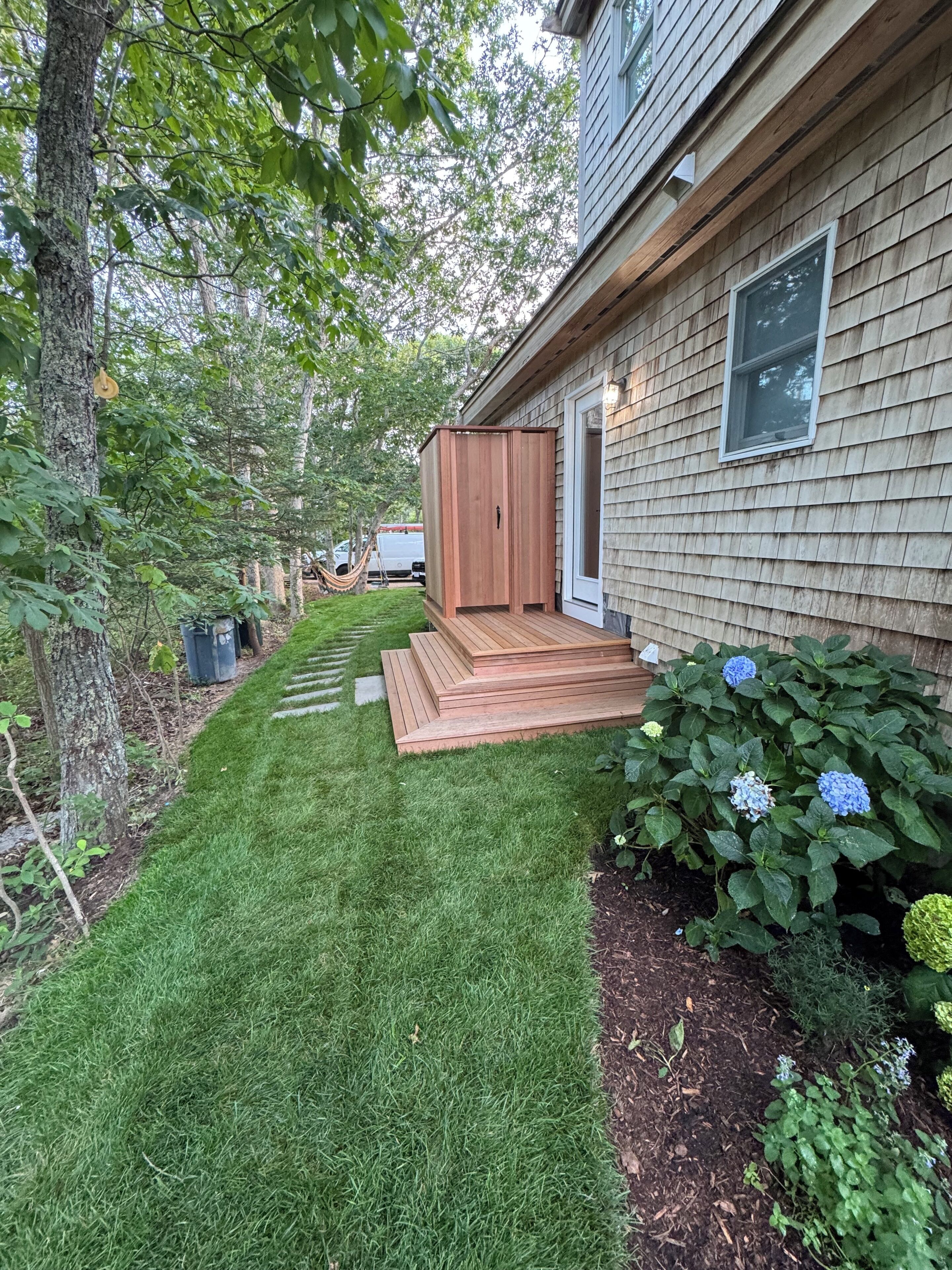Une propriété résidentielle dotée d’une terrasse en bois, d’un petit abri de jardin et d’une pelouse bien entretenue.