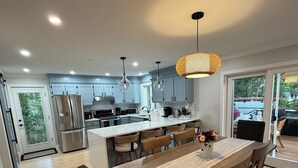 A modern kitchen with a central island, stainless steel appliances, and a dining area with a wooden table and chairs. - Spacious, Family-Friendly Edgartown Home – 3BR, Sleeps 14, Renovated in 2025 (Edgartown)