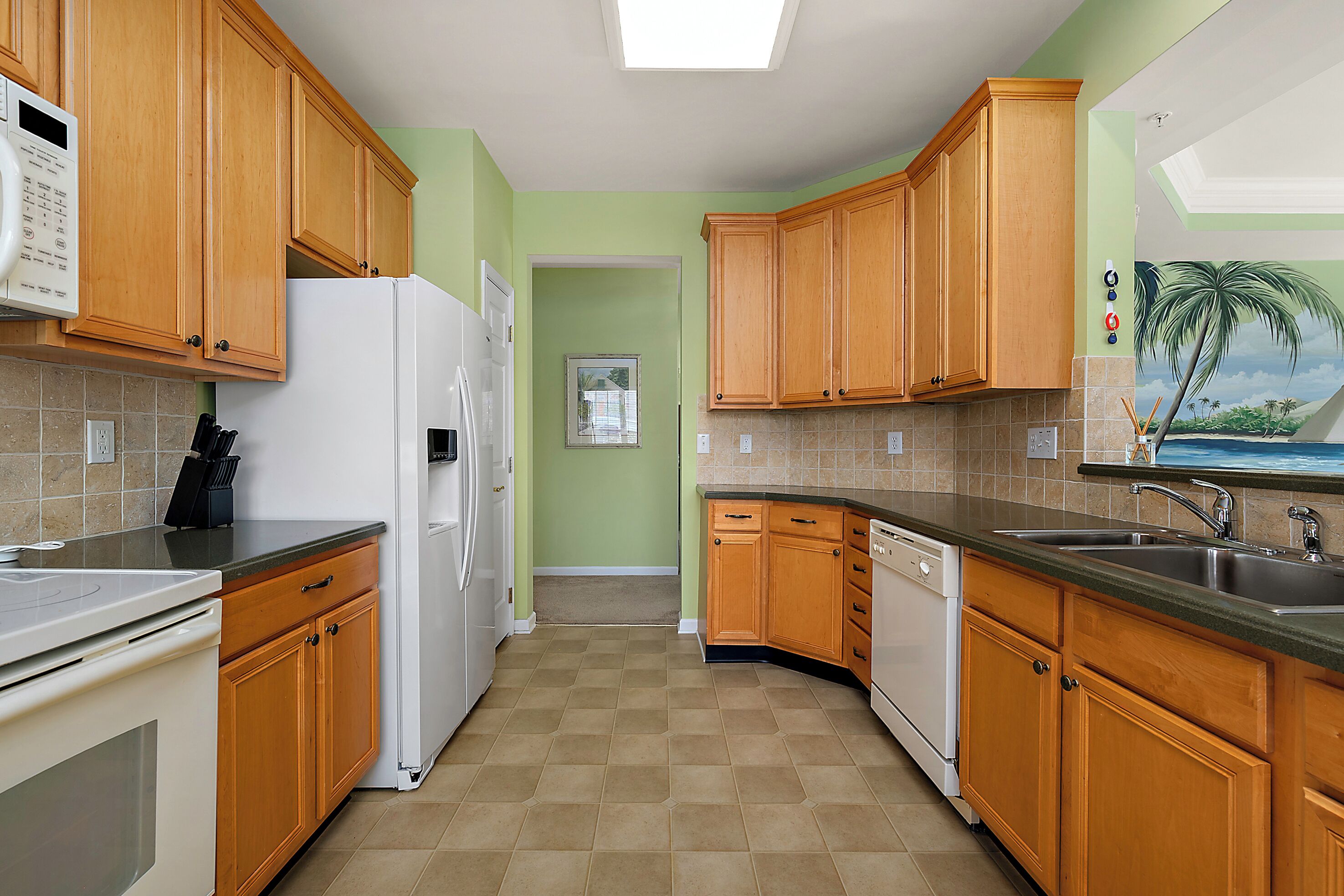 Una cocina con armarios de madera, un refrigerador blanco, un lavavajillas y piso de baldosas.