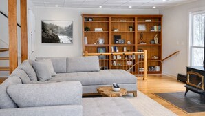 A modern living room with a grey sectional sofa, wooden bookshelves, and a fireplace.