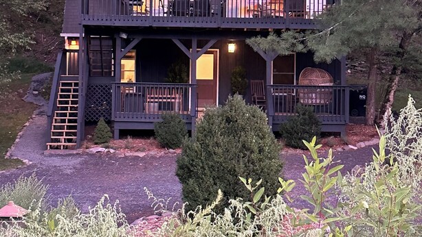 A two-story cabin with a balcony on each floor, surrounded by trees.