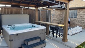 Ein Whirlpool mit Stufen und einem Holztisch mit Stühlen, eingebettet in einen Hinterhof mit Backsteinmauer und Holzlattenzaun.