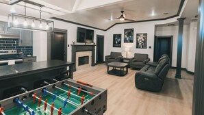 Ein geräumiges Wohnzimmer mit einem Kicker, einem Kamin und einer modernen Küche im Hintergrund.