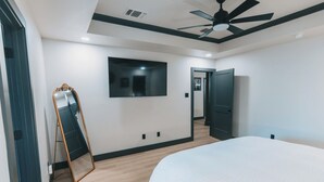 Ein Schlafzimmer mit Bett, Deckenventilator, Fernseher und einer Tür.