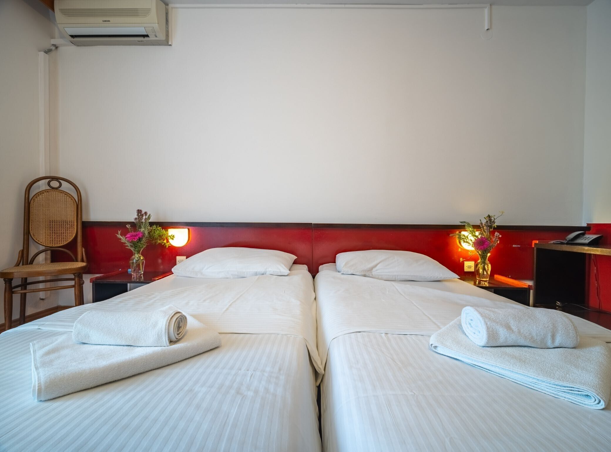 Une chambre d’hôtel avec deux lits, une chaise, un bureau, un téléphone et un vase avec des fleurs.