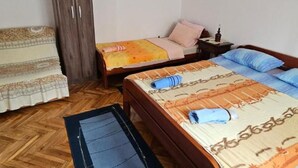 Un dormitorio con dos camas, piso de madera, un armario y una mesita con lámpara.
